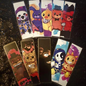 May include: A collection of colorful, illustrated bookmarks featuring characters from a popular video game series. The bookmarks showcase various characters in vibrant colors, including a purple bunny with a guitar, a yellow chick with a bib, and a red bear with an eyepatch.