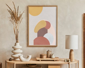 May include: A framed abstract art print with a wooden frame, featuring a design of overlapping shapes in muted colours. A white vase with dried plants, a wooden lamp, and decorative items are on a wooden console table.