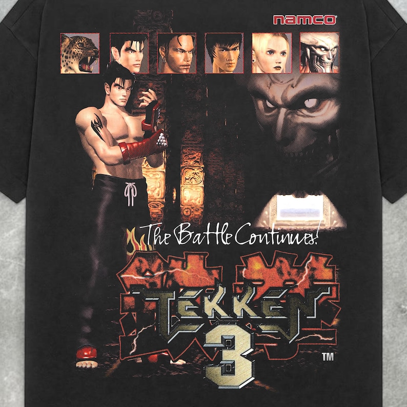 May include: Black t-shirt featuring a graphic from the Tekken 3 video game. The design includes character portraits, the game's logo, and the phrase "The Battle Continues!". The Namco logo is at the top.