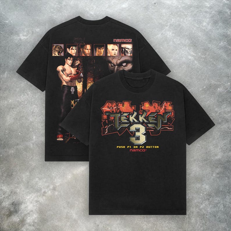 May include: Two black t-shirts featuring graphics from the Tekken 3 video game. One shirt displays character portraits and a central image, while the other showcases the game's logo and the text "PUSH P1 OR P2 BUTTON namco".
