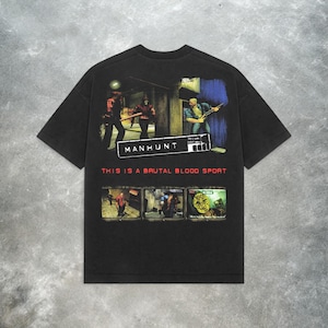 Peut inclure: T-shirt noir avec un imprim&eacute; graphique d'un personnage de jeu vid&eacute;o tenant une arme. Le texte "Manhunt" et "This is a brutal blood sport" est imprim&eacute; sur le t-shirt.