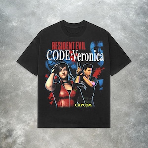 May include: Black t-shirt featuring the Resident Evil Code: Veronica video game. The design includes the game's title in red and white, along with character illustrations. The Capcom logo is visible at the bottom.