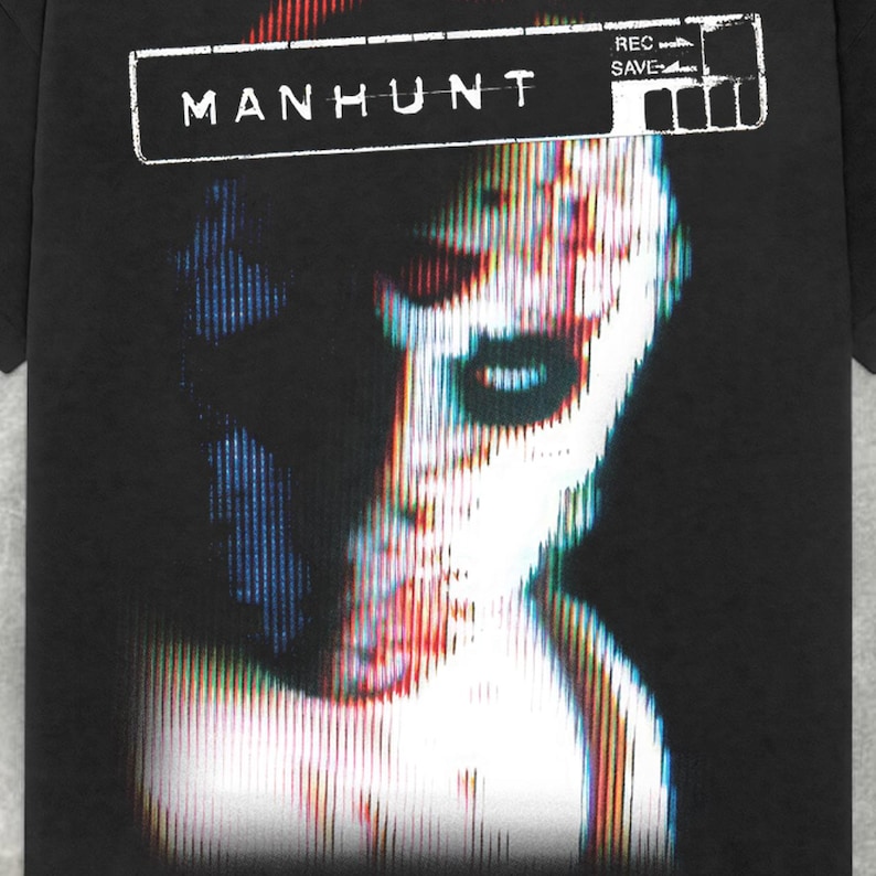 Peut inclure: T-shirt noir avec un motif blanc d'un visage &agrave; l'effet pixelis&eacute;. Le texte "MANHUNT" est au-dessus du motif et "REC SAVE" est &agrave; droite du motif.