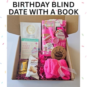 May include: A gift box labeled "BIRTHDAY BLIND DATE WITH A BOOK" filled with various items. Includes a pink face mask, eye patches, Milano cookies, a pink pen, a coaster with a cupcake design, pink socks, and other pink-themed items.