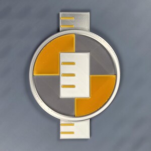 May include: A 3D-printed, circular object with a clear center, bordered by a silver ring. It features white and yellow geometric shapes, with a silver rectangular extension at the top and bottom, each with three parallel lines.