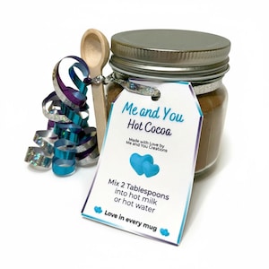 Peut inclure: Un pot de mélange pour chocolat chaud avec un couvercle argenté, une cuillère en bois et une étiquette cadeau indiquant "Me and You Hot Cocoa". L'étiquette comprend des instructions et un motif de cœur. Ruban décoratif bleu et argenté inclus.
