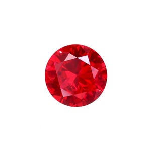 May include: A round, faceted, brilliant red gemstone. The gem is a vibrant, saturated red colour and appears to be cut with many facets to maximise light reflection. The gemstone is set against a plain white background.