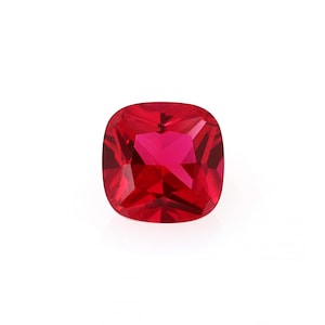 May include: A deep red cushion-cut gemstone with a faceted surface.