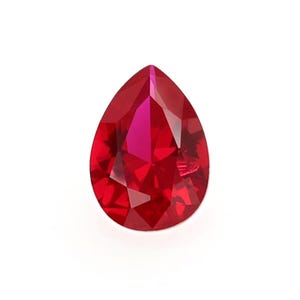 May include: A pear-shaped ruby gemstone with a deep red color and a faceted cut.