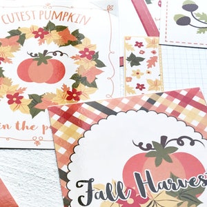 May include: A collection of fall-themed paper cutouts. One cutout features a pumpkin surrounded by a wreath of leaves and the text "Cutest Pumpkin in the patch." Another says "Fall Harvest" with a pumpkin and leaves.