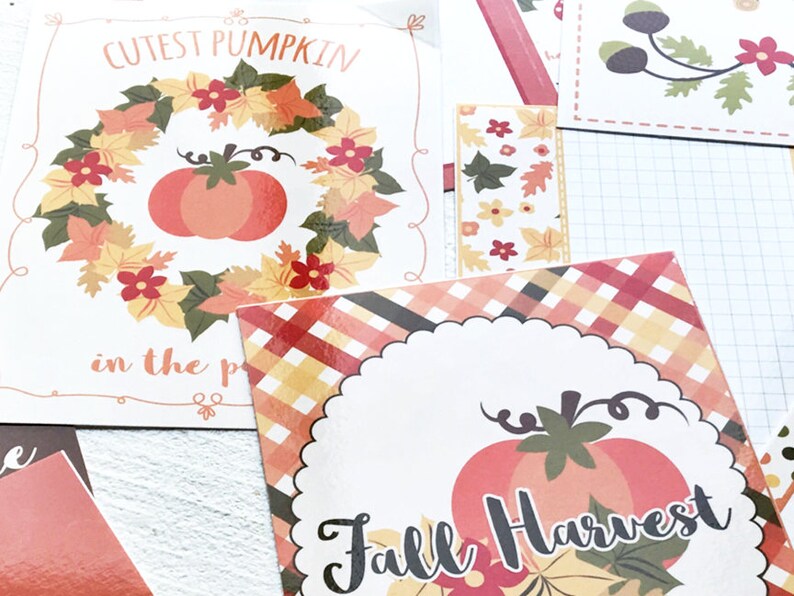 May include: A collection of fall-themed paper cutouts. One cutout features a pumpkin surrounded by a wreath of leaves and the text "Cutest Pumpkin in the patch." Another says "Fall Harvest" with a pumpkin and leaves.