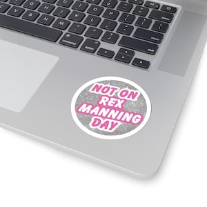 Op de afbeelding: Een zilveren glitter sticker met een roze cirkel waarop staat "Niet op Rex Manning Day".