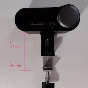 May include: A black SteelSeries audio controller with a large gray dial and a mounting clamp. The controller is 2 inches (51 mm) tall and 1 inch (25 mm) wide.