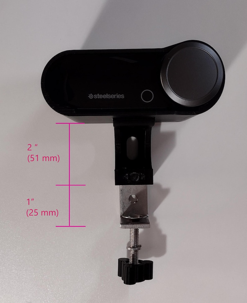 May include: A black SteelSeries audio controller with a large gray dial and a mounting clamp. The controller is 2 inches (51 mm) tall and 1 inch (25 mm) wide.