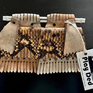 May include: A brown and gold leather fringe purse with a snake skin pattern and a Play Dead tag. The tag says "one of a kind, hand crafted, made in the USA".