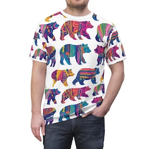 Op de afbeelding: Wit T-shirt met een patroon van kleurrijke beren. Elke beer is versierd met ingewikkelde patronen in roze, blauw, oranje en groen. Het shirt heeft een ronde hals en korte mouwen.