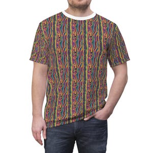 Op de afbeelding: Een t-shirt met korte mouwen met een levendig, verticaal gestreept patroon in tinten paars, blauw, geel en rood. De shirt heeft een witte ronde hals en wordt gedragen door een persoon in een blauwe jeans.