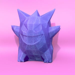 May include: A purple, geometric-shaped figure with a smiling face, two small arms, and spiky protrusions on its head. The figure is set against a pink background, creating a vibrant contrast. The design has a textured appearance.