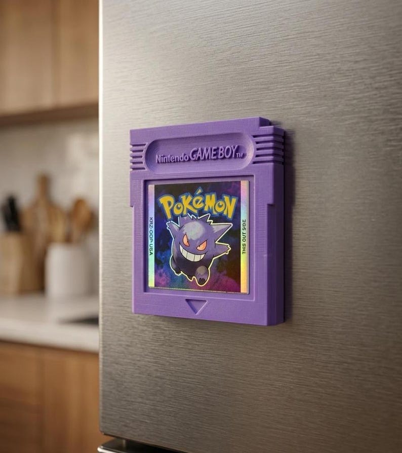 May include: A purple Game Boy cartridge magnet featuring the Pok&eacute;mon Gengar. The magnet has the Nintendo Game Boy logo and the Pok&eacute;mon logo. The cartridge is attached to a stainless steel surface.