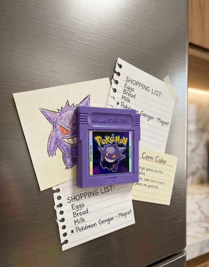 May include: A purple Nintendo Game Boy cartridge magnet featuring the Pok&eacute;mon Gengar, alongside handwritten shopping lists and a drawing of Gengar. The lists include items like eggs, bread, and milk.
