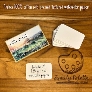 Puede incluir: Un conjunto de materiales de arte, que incluye una caja etiquetada como "petite palette" con una pintura de paisaje, una pila de tarjetas en blanco y una paleta de madera. La caja contiene 25 papeles de acuarela de 3,18 x 5,08 cm.