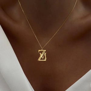 Op de afbeelding: Een gouden ketting met een hanger met de letters "ZM" in een vet, gestileerd lettertype.
