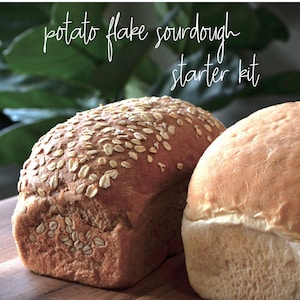 Può includere: Due pagnotte di pane, una con una crosta marrone chiaro e l'altra con una crosta marrone scuro e fiocchi d'avena in cima. Il testo "potato flake sourdough starter kit" è scritto sopra le pagnotte di pane.