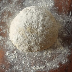 May include: A close-up of a round ball of dough covered in white flour on a wooden surface.