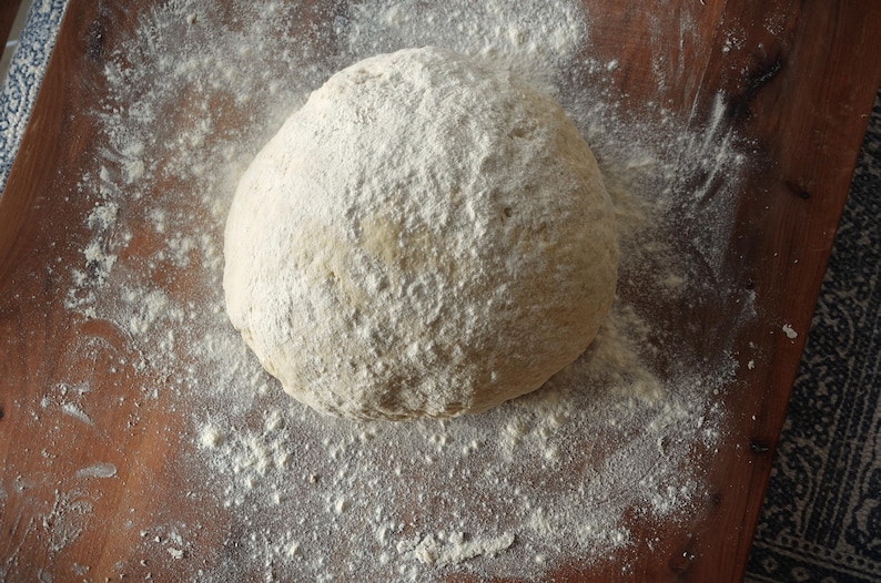 May include: A close-up of a round ball of dough covered in white flour on a wooden surface.