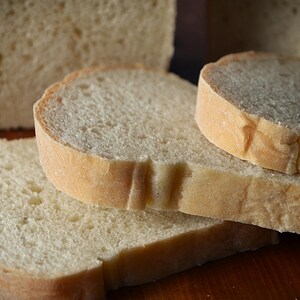 May include: Four slices of white bread stacked on top of each other. The bread is soft and fluffy, with a slightly golden crust.