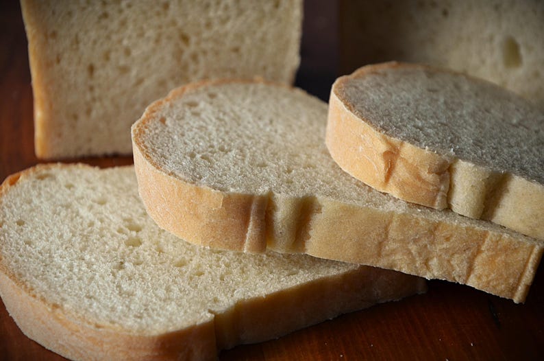 May include: Four slices of white bread stacked on top of each other. The bread is soft and fluffy, with a slightly golden crust.