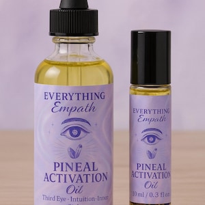 May include: Two glass bottles of Pineal Activation Oil. The larger bottle has a dropper, and the smaller one is a rollerball. Both bottles have a purple label with the words "EVERYTHING Empath" and "PINEAL ACTIVATION Oil". The labels also feature an eye and a crystal design.