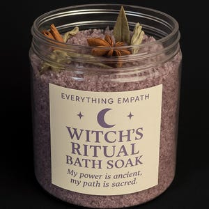 May include: A clear plastic jar filled with purple bath soak. The jar has a label that reads "Witch's Ritual Bath Soak." The soak is topped with star anise, cinnamon sticks, and other botanicals. The text on the label reads "Everything Empath, My power is ancient, my path is sacred."