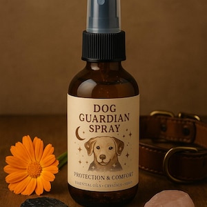 May include: A brown glass bottle of Dog Guardian Spray with a black cap and spray nozzle. The label features a dog illustration, the text "Protection & Comfort", and the words "Essential Oils, Crystals, Heres". An orange flower, a black stone, a rose quartz, and a leather dog collar are also visible.