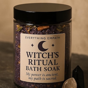 Pode incluir: Um frasco de vidro com tampa preta cheio de sais de banho roxos. O rótulo diz "Witch's Ritual Bath Soak" com o texto "My power is ancient, my path is sacred". Dois cristais estão ao lado do frasco.