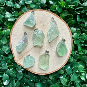 May include: Seven green fluorite crystal pendants with silver bail settings. The pendants are displayed on a wooden surface.