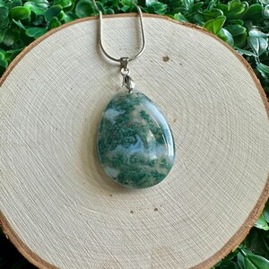 May include: A silver chain necklace with a green and white agate pendant. The pendant is a teardrop shape and has a swirling pattern of green and white.