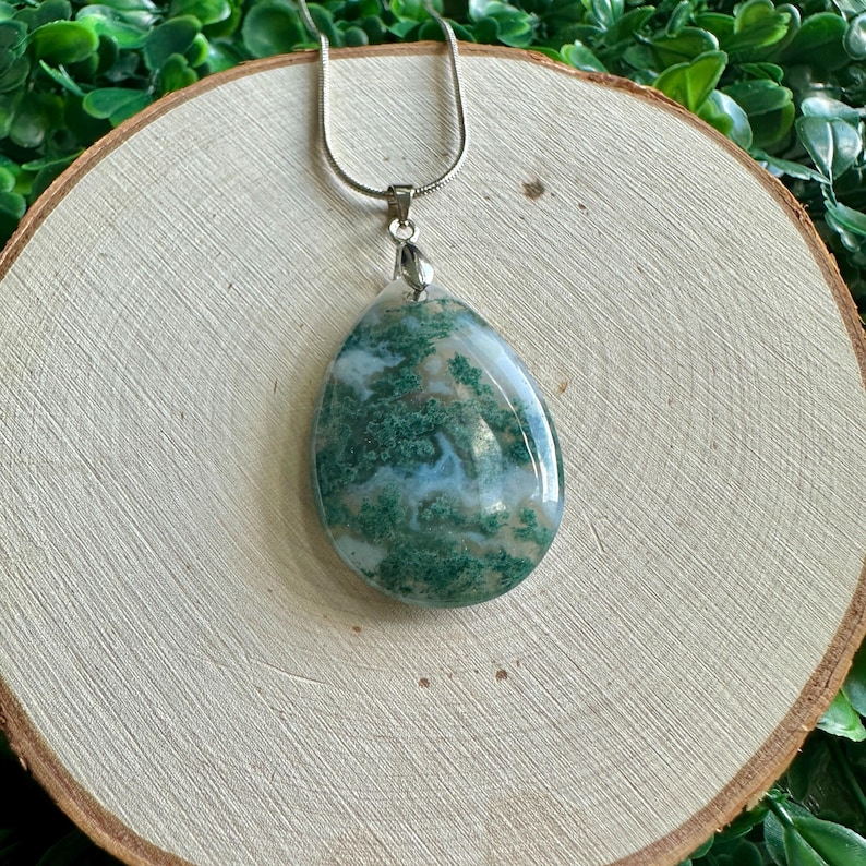 May include: A silver chain necklace with a green and white agate pendant. The pendant is a teardrop shape and has a swirling pattern of green and white.