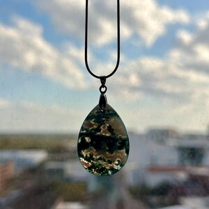 May include: A silver chain necklace with a teardrop-shaped pendant made of green and white agate. The pendant has a cloudy, swirling pattern.