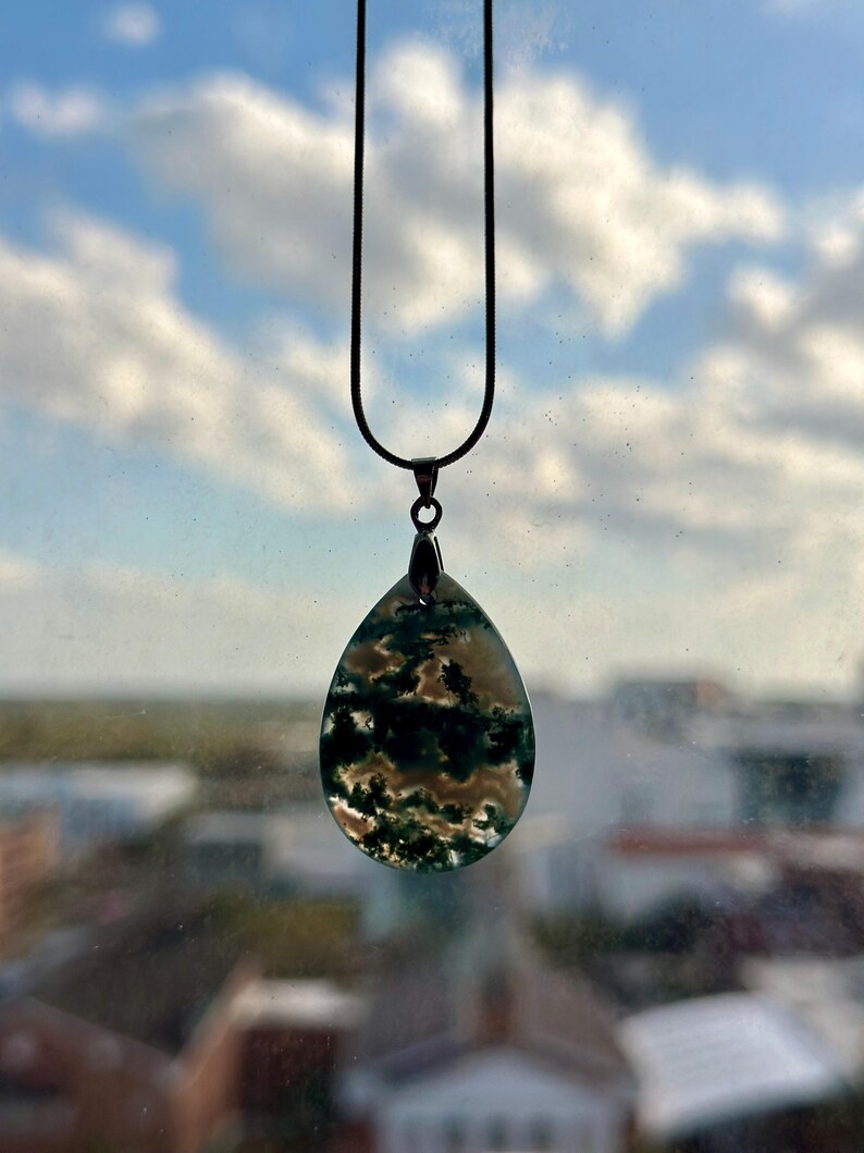May include: A silver chain necklace with a teardrop-shaped pendant made of green and white agate. The pendant has a cloudy, swirling pattern.