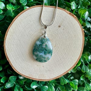 May include: A silver chain necklace with a green and white moss agate pendant in the shape of a teardrop.