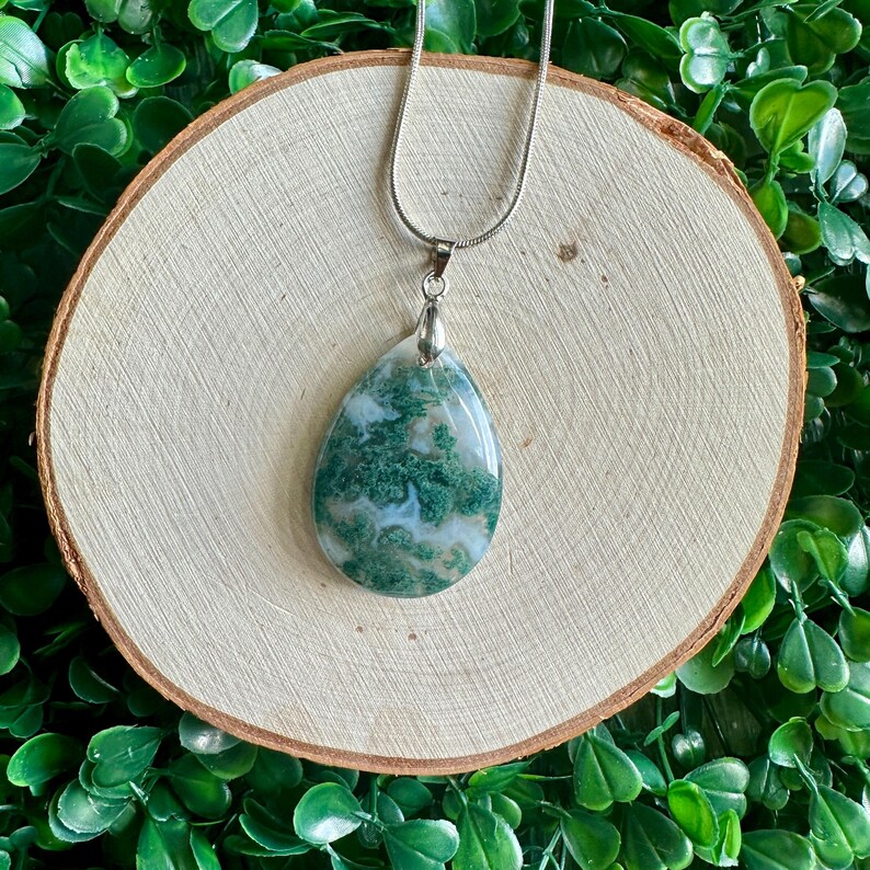 May include: A silver chain necklace with a green and white moss agate pendant in the shape of a teardrop.