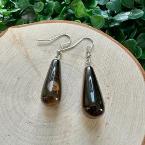 May include: A pair of teardrop-shaped earrings with silver hooks. One earring is black with a brown swirl inside, and the other is solid black.