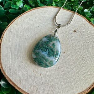 May include: A green and white agate pendant on a silver chain. The pendant is teardrop shaped and has a natural, organic look.