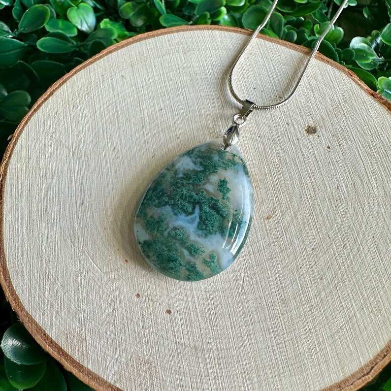 May include: A green and white agate pendant on a silver chain. The pendant is teardrop shaped and has a natural, organic look.