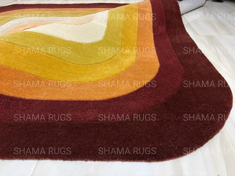 May include: A colorful, retro-style rug with a layered design. The rug features curved bands of color, including cream, yellow, orange, and burgundy. The rug is made of a soft, plush material and is suitable for a living room or bedroom.