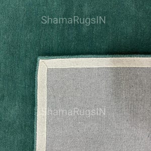 Puede incluir: Primer plano de una alfombra verde azulado con un borde blanco y un reverso gris. El texto "ShamaRugsIN" es visible en la superficie de la alfombra. La alfombra tiene una textura suave y afelpada.