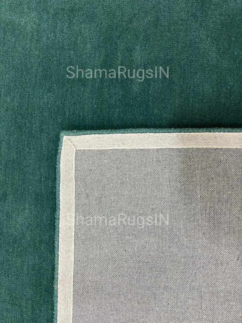 Puede incluir: Primer plano de una alfombra verde azulado con un borde blanco y un reverso gris. El texto "ShamaRugsIN" es visible en la superficie de la alfombra. La alfombra tiene una textura suave y afelpada.
