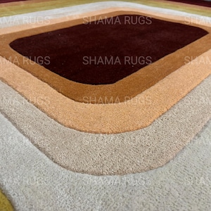 May include: A geometric rug with a diamond-shaped design. The rug features concentric layers of color, including shades of brown, beige, and gray. The text "SHAMA RUGS" is visible in the image.