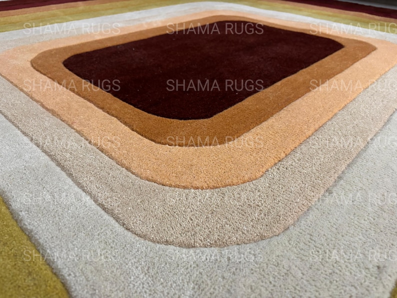 May include: A geometric rug with a diamond-shaped design. The rug features concentric layers of color, including shades of brown, beige, and gray. The text "SHAMA RUGS" is visible in the image.